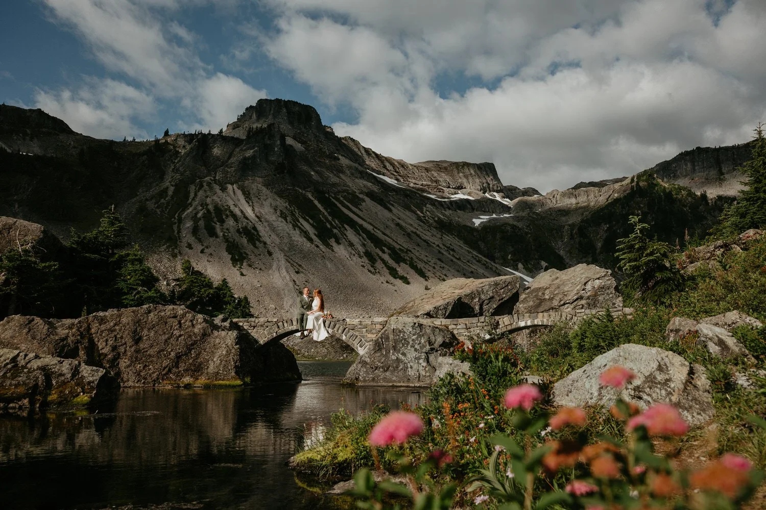 Couple sitting on a stone footbridge over Bagley Lakes surrounded by blooming wildflowers
