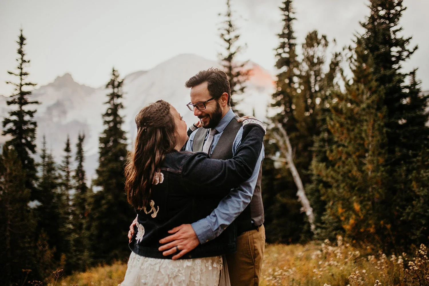 Eloping couple embracing in a forest clearing with soft mountain views and evergreen trees in the background
