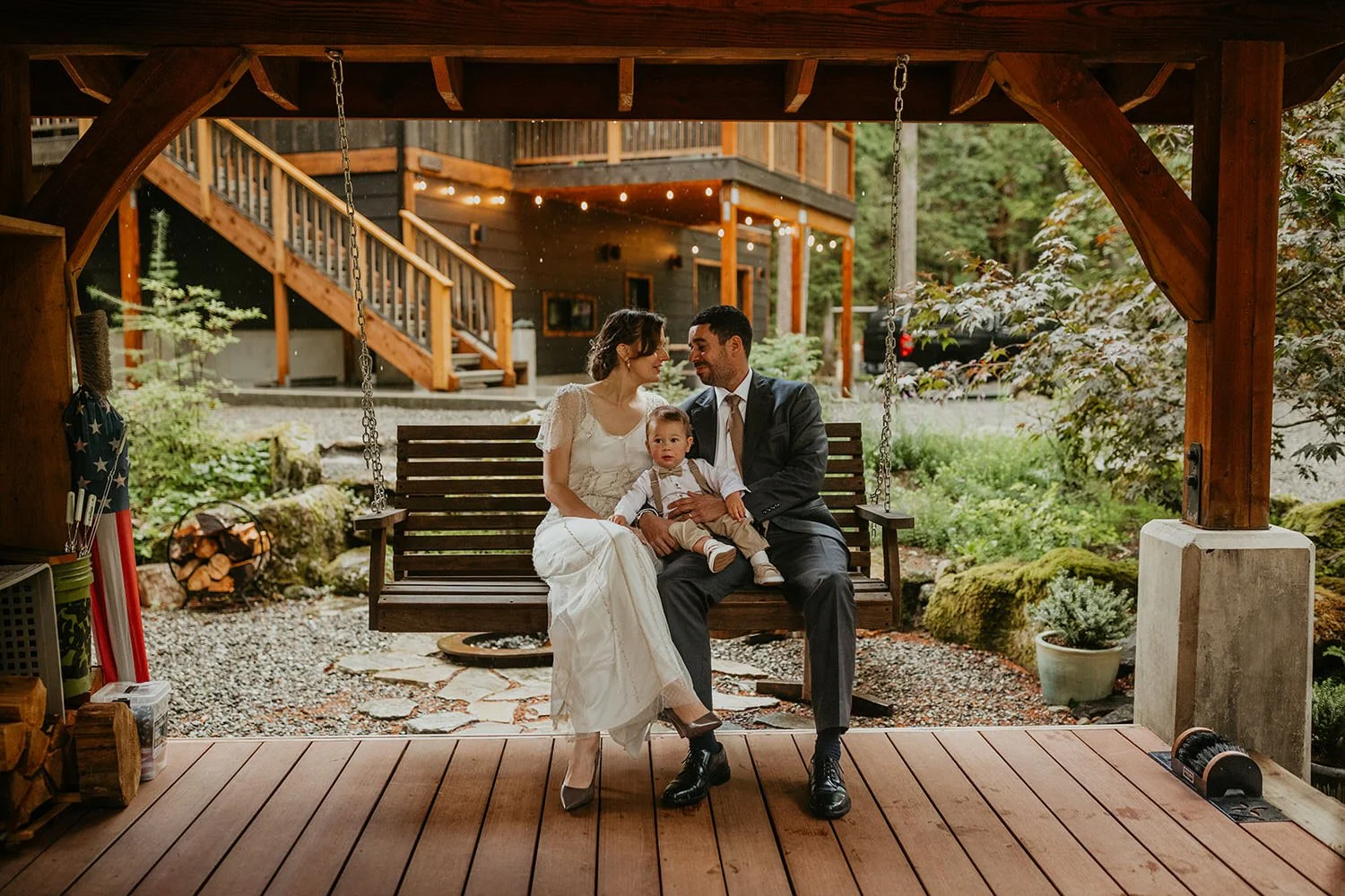 Eloping couple and their baby sitting together on a wooden porch at a North Cascades cabin, sharing a quiet moment after their ceremony