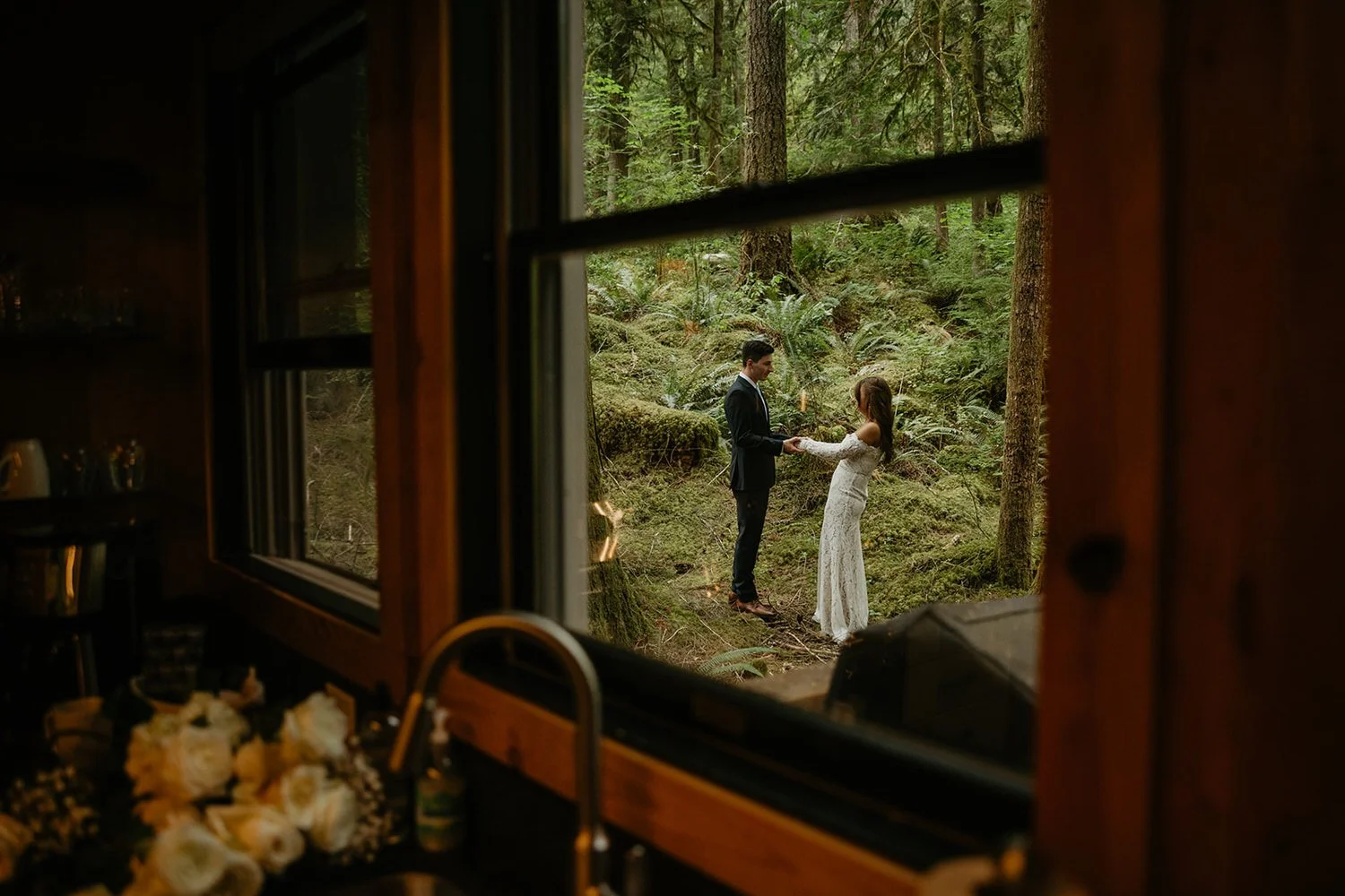 Couple photographed through a cabin window during their Washington elopement, warm interior light framing an intimate moment