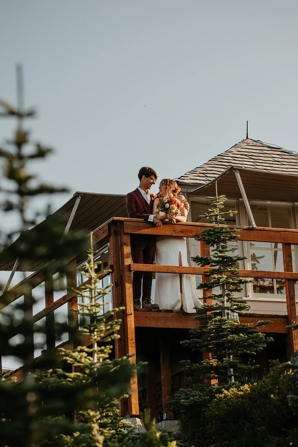 Couple relaxing on a fire lookout deck in Washington, overlooking trees and mountains during an elopement day