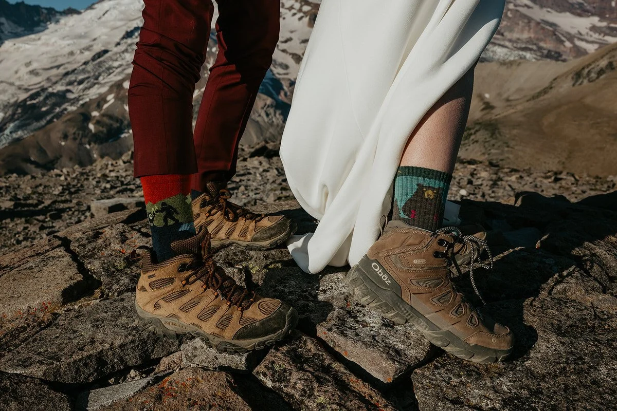 Close-up of a couple wearing hiking boots and patterned socks on a rocky mountain summit during a Washington hiking elopement.