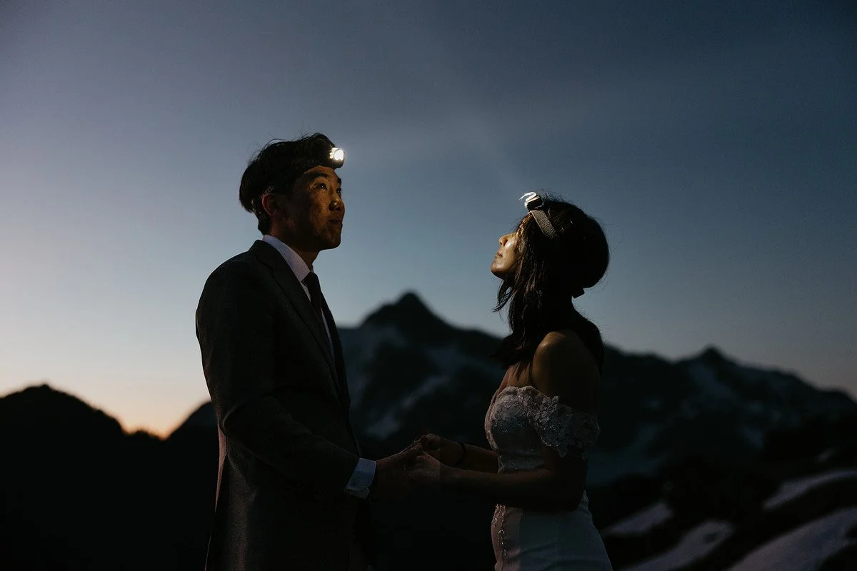 Couple hold hands wearing headlamps at dusk in the mountains during a twilight Washington elopement adventure.