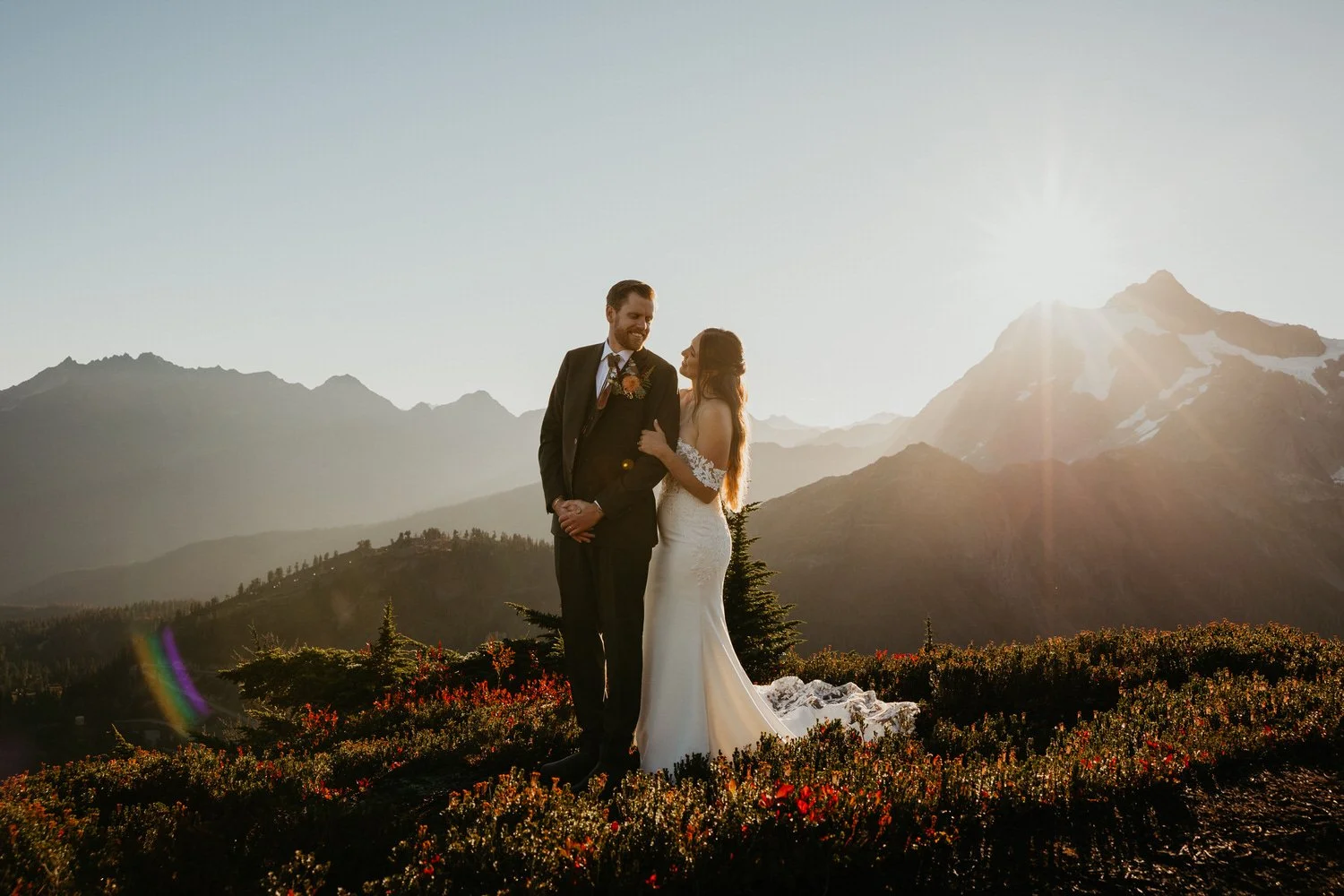 Couple standing in an alpine meadow at sunset with mountain views during a Washington elopement.