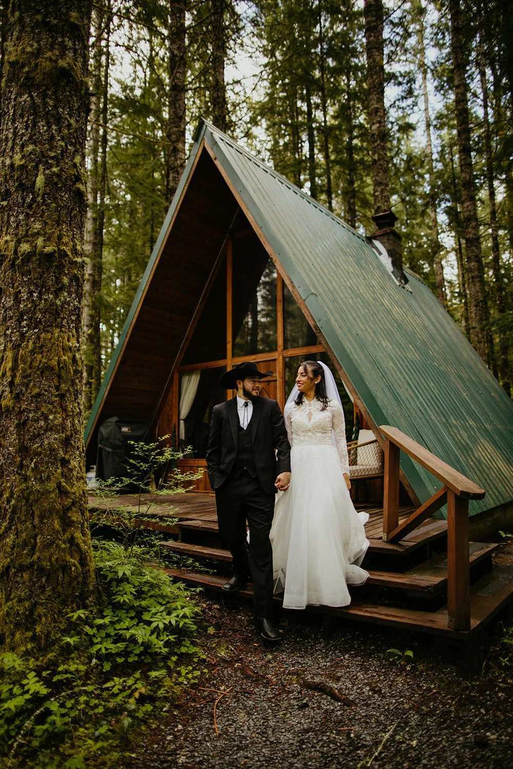 Eloping couple walking hand in hand off the deck of a green A-frame cabin during their Washington elopement