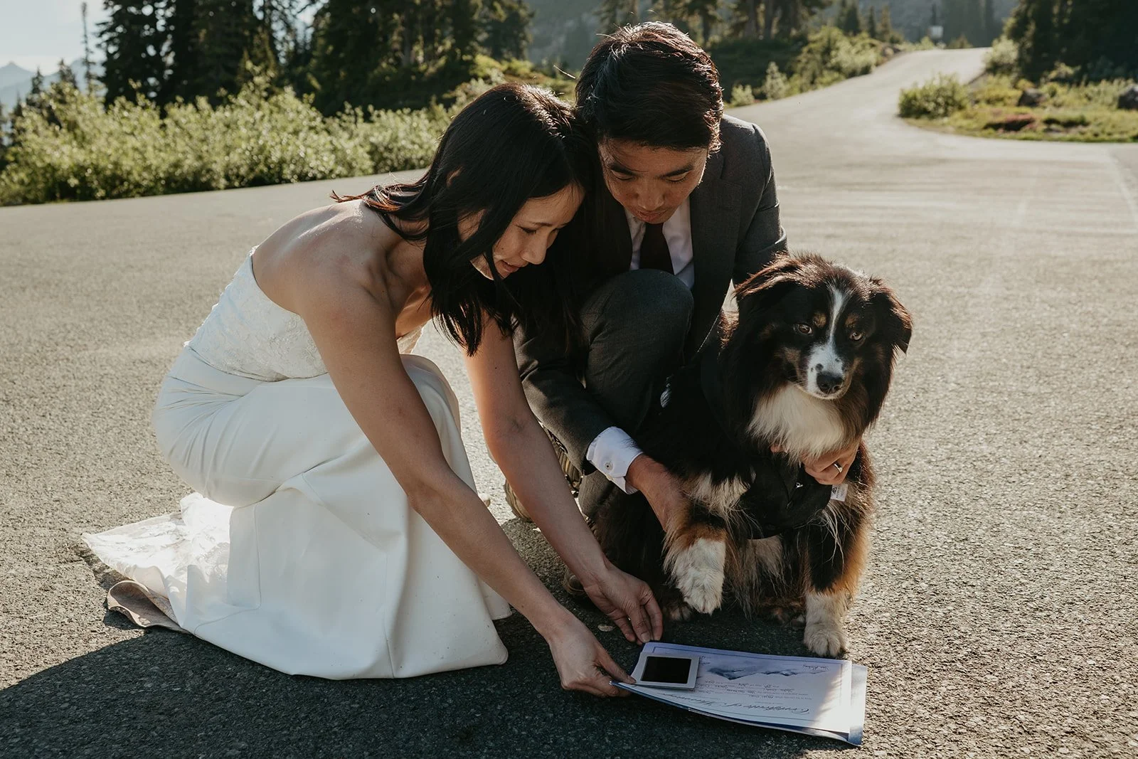 Couple crouched on pavement signing their marriage certificate with their dog looking on