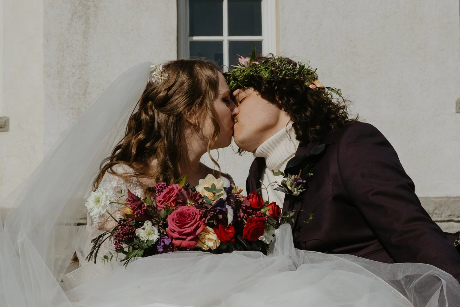 Newly married couple sharing a kiss while holding a colorful bouquet during their wedding day.