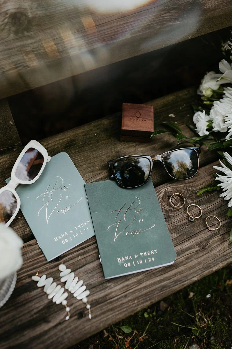 Elopement detail flat lay featuring vow books, rings, florals, and personal accessories.