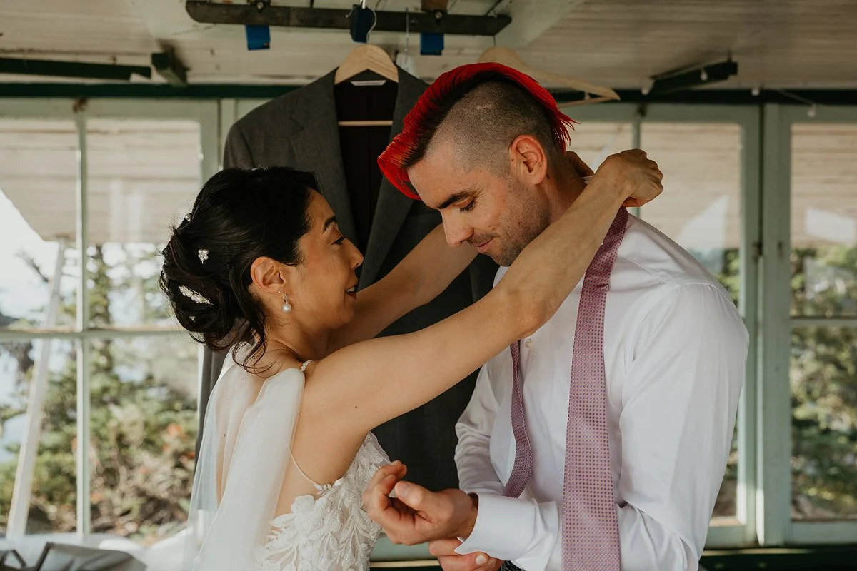 Bride helping groom adjust his tie inside a cozy cabin before their Washington hiking elopement.
