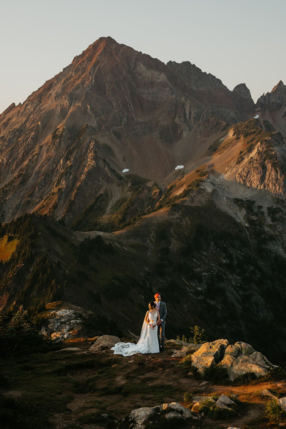 Bride and groom standing alone in a flowing wedding dress in the North Cascades, surrounded by rugged mountain terrain and early morning light