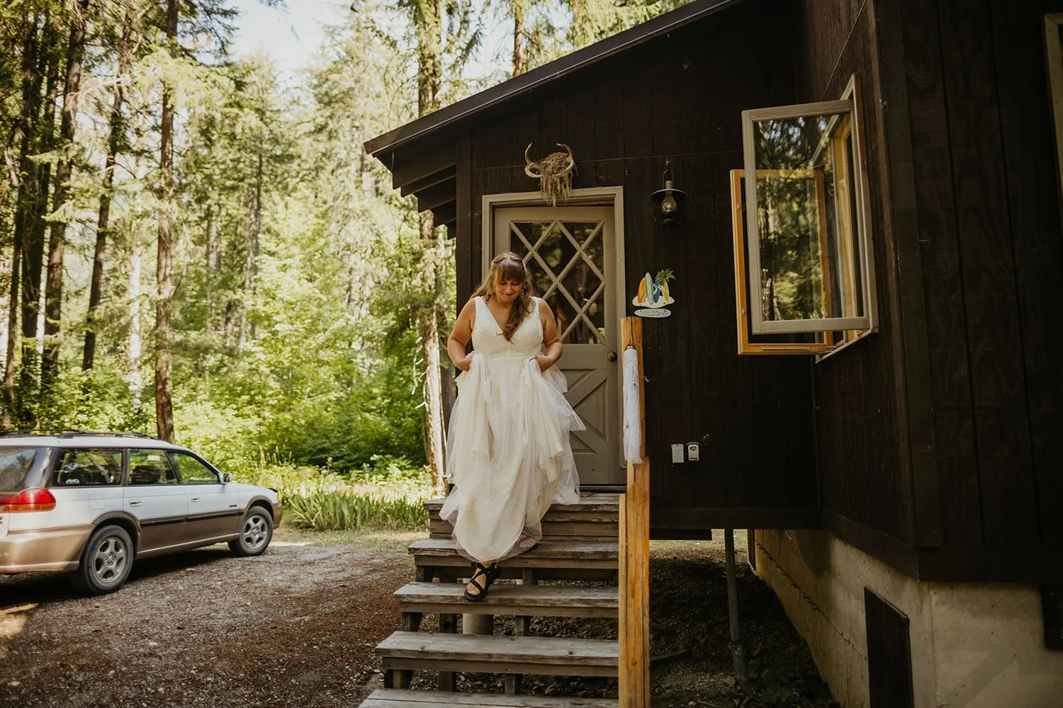 Bride in wedding dress makes her way down the cabin steps to meet her groom in a rustic Stehekin cabin
