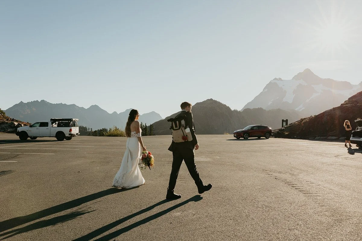 Newly married couple walking through a mountain parking lot with other cars and visitors nearby in Washington