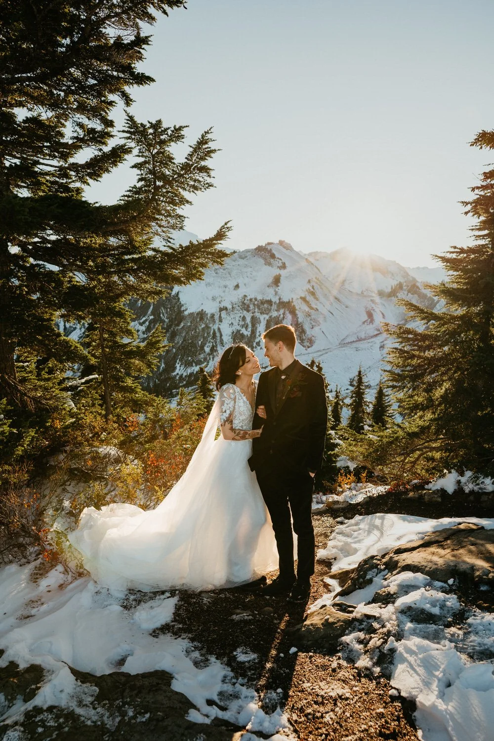 Couple embracing among snow and fall foliage with mountain sunlight breaking through evergreen trees