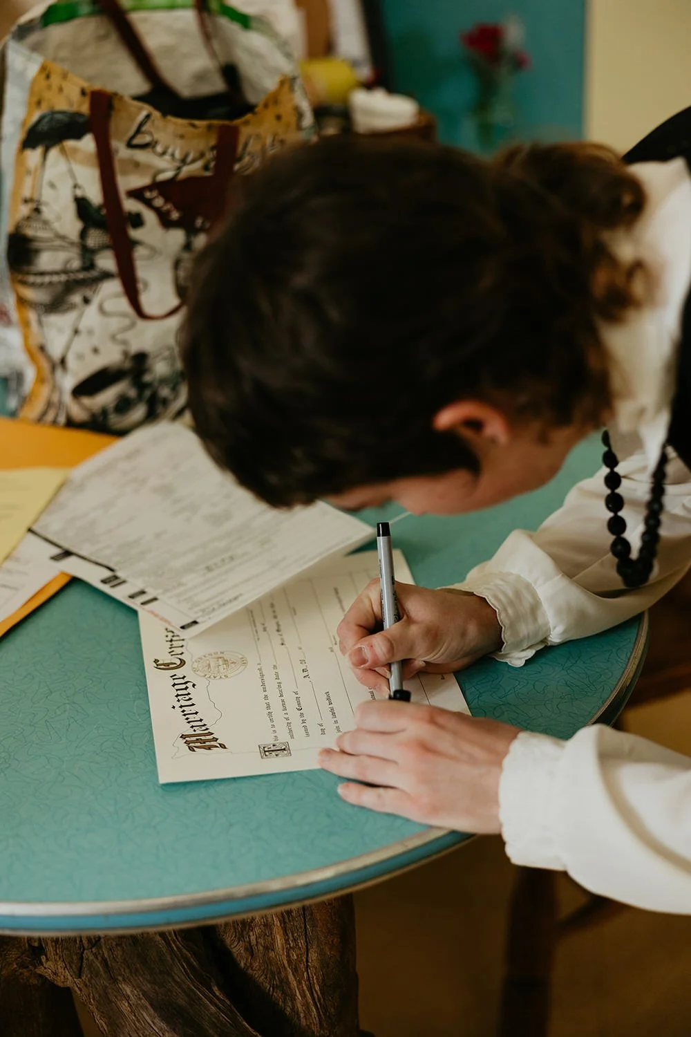 Close-up of hands signing a Washington State marriage license on an elopement day, with a beaded bracelet visible