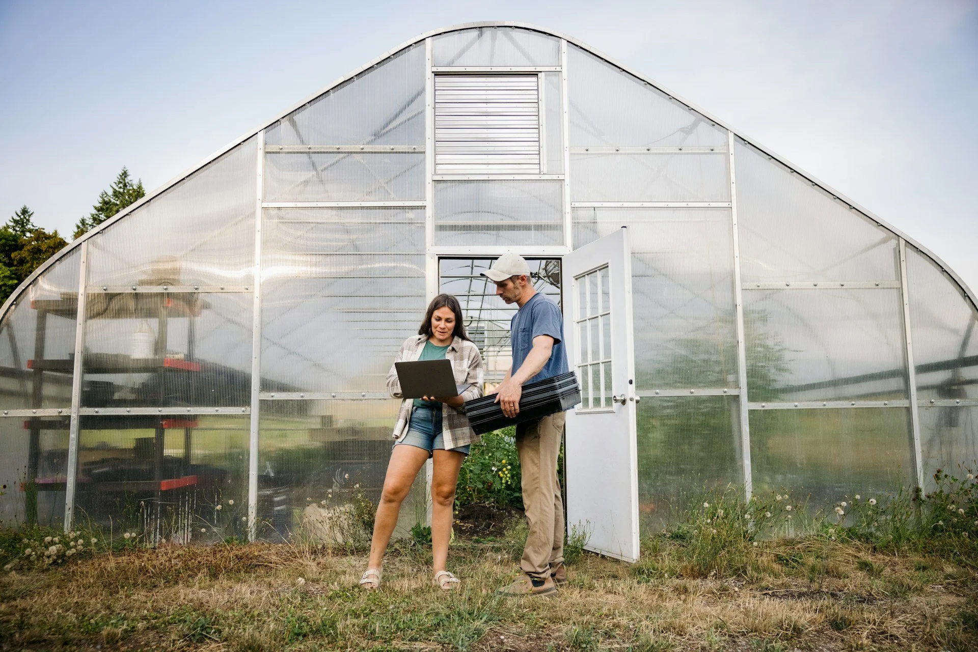 two people consulting on a farm in front of a greenhouse