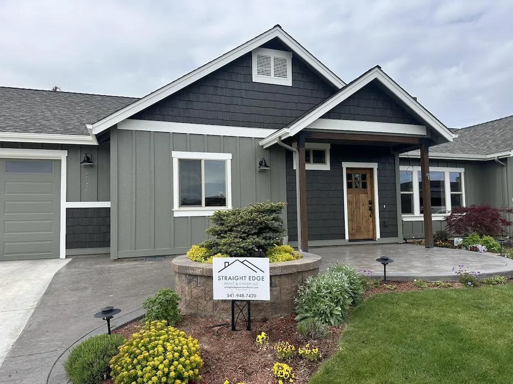 Exterior painting in Prineville Oregon with deep green gray siding black gables white trim and a natural wood front door by Straight Edge Paint & Finish LLC