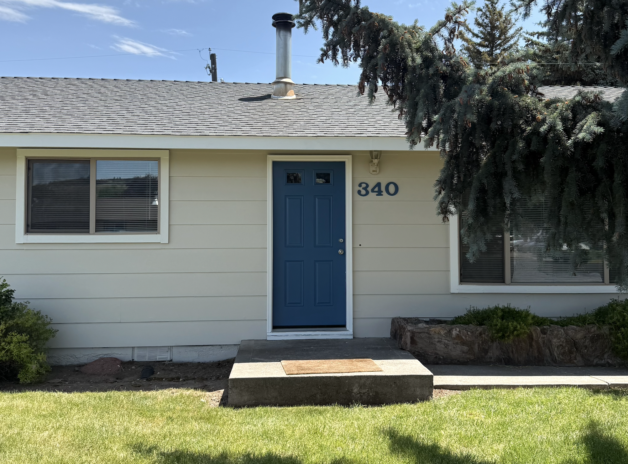 Freshly painted single-story home in Prineville, Oregon featuring cream-colored siding and a bold blue front door, completed by Straight Edge Paint and Finish.