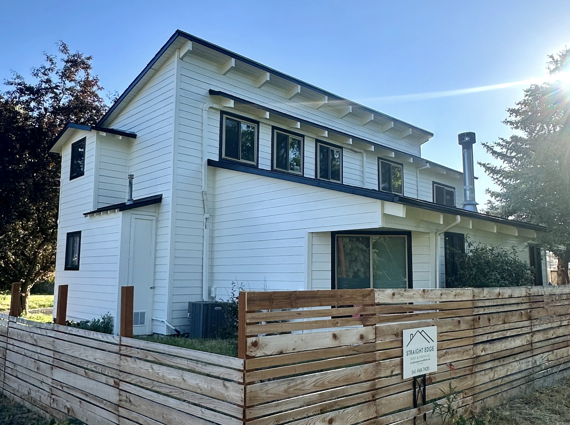 Modern white two-story home with black trim and a natural wood fence, freshly painted by Straight Edge Paint and Finish in Central Oregon.