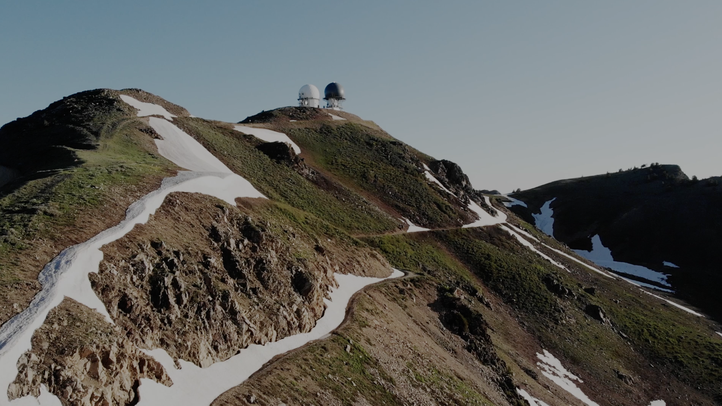 Francis Peak with snow patches on a mountain with radar domes at the summit under clear sky.