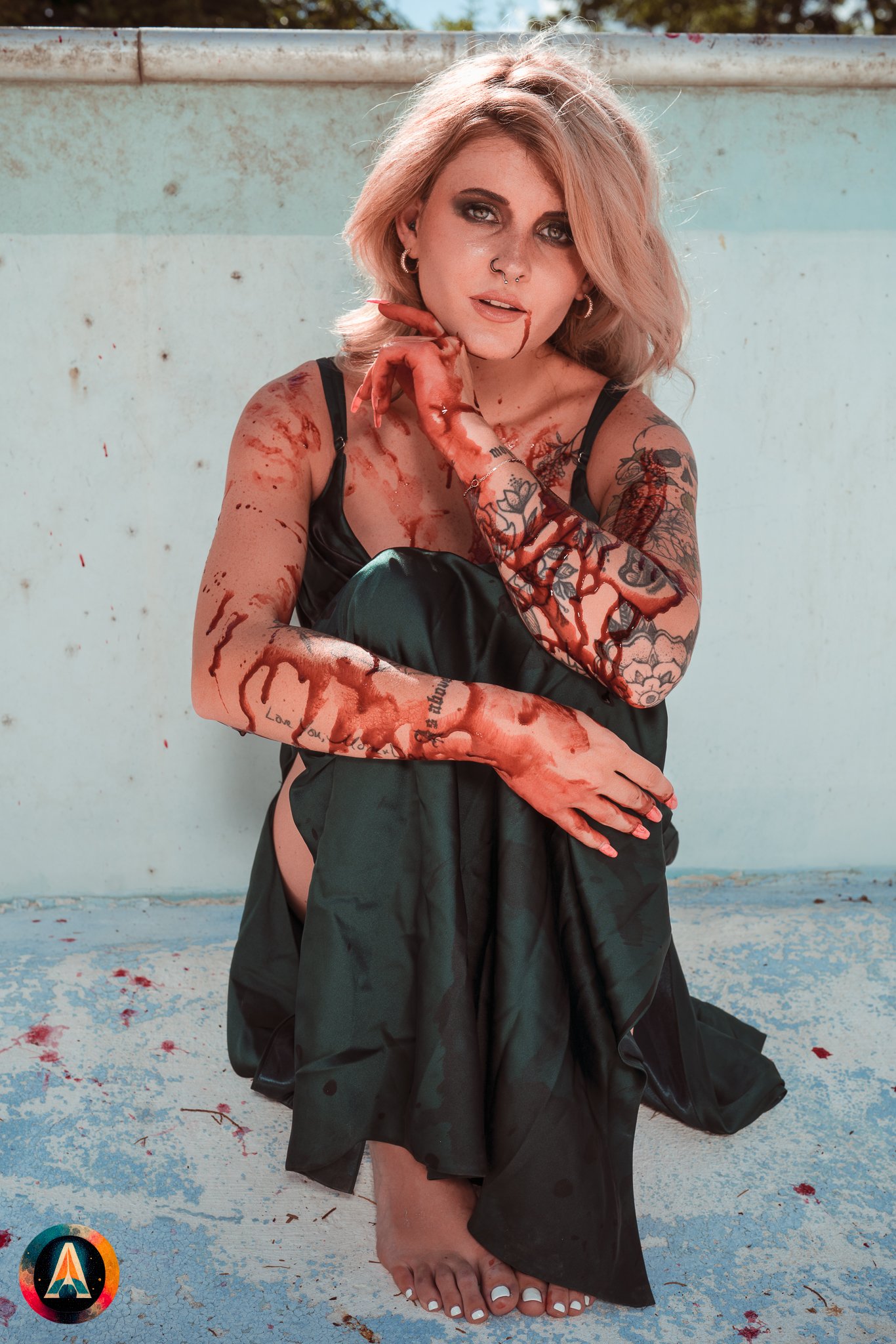 Blonde model courtney france poses in the haunted indiana state sanitarium pool in a elegant black / green dress covered in fake blood.