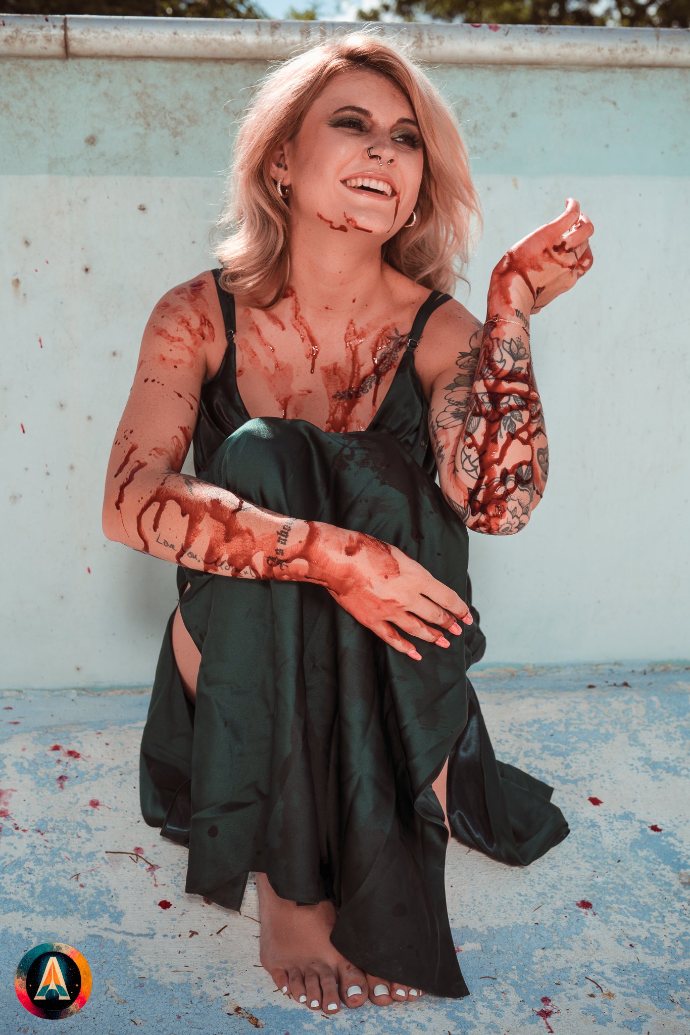 Blonde model courtney france poses in the haunted indiana state sanitarium pool in a elegant black / green dress covered in fake blood.
