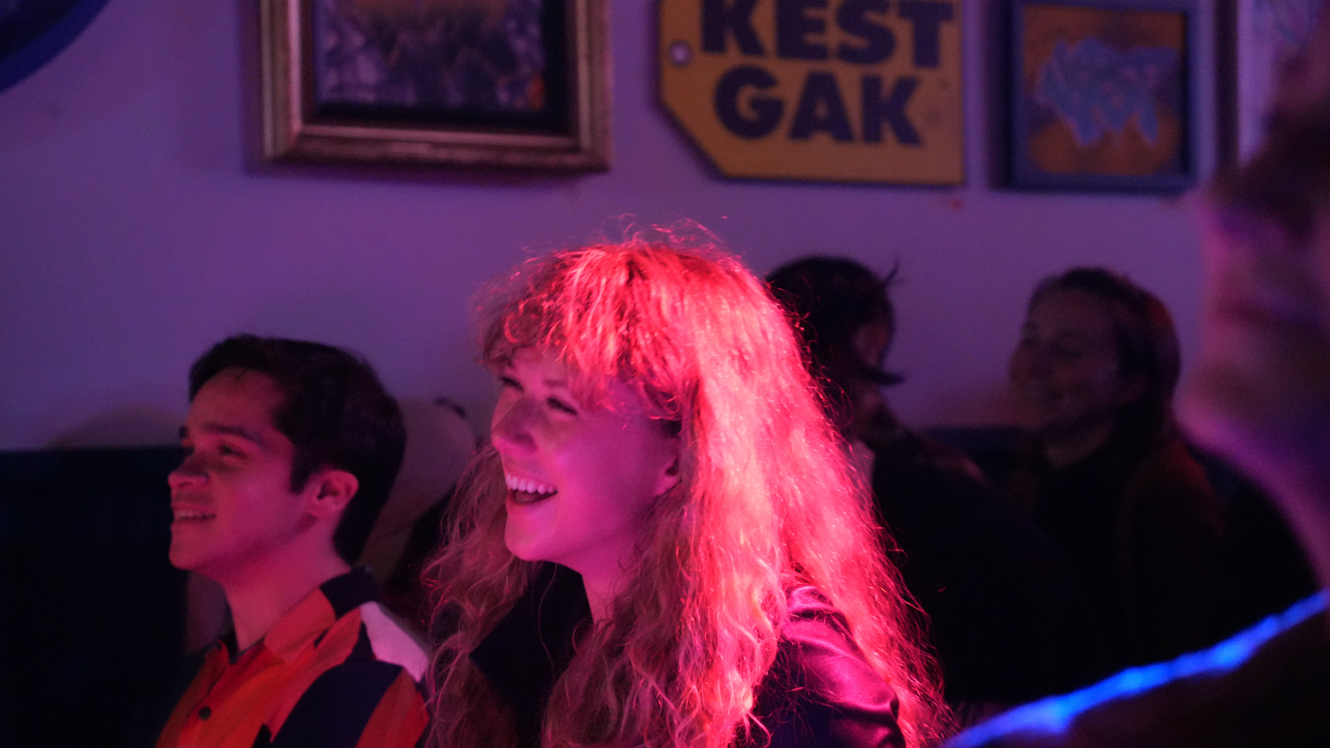 People at a bar or nightclub laughing and enjoying themselves with colorful lighting, and framed pictures on the wall.