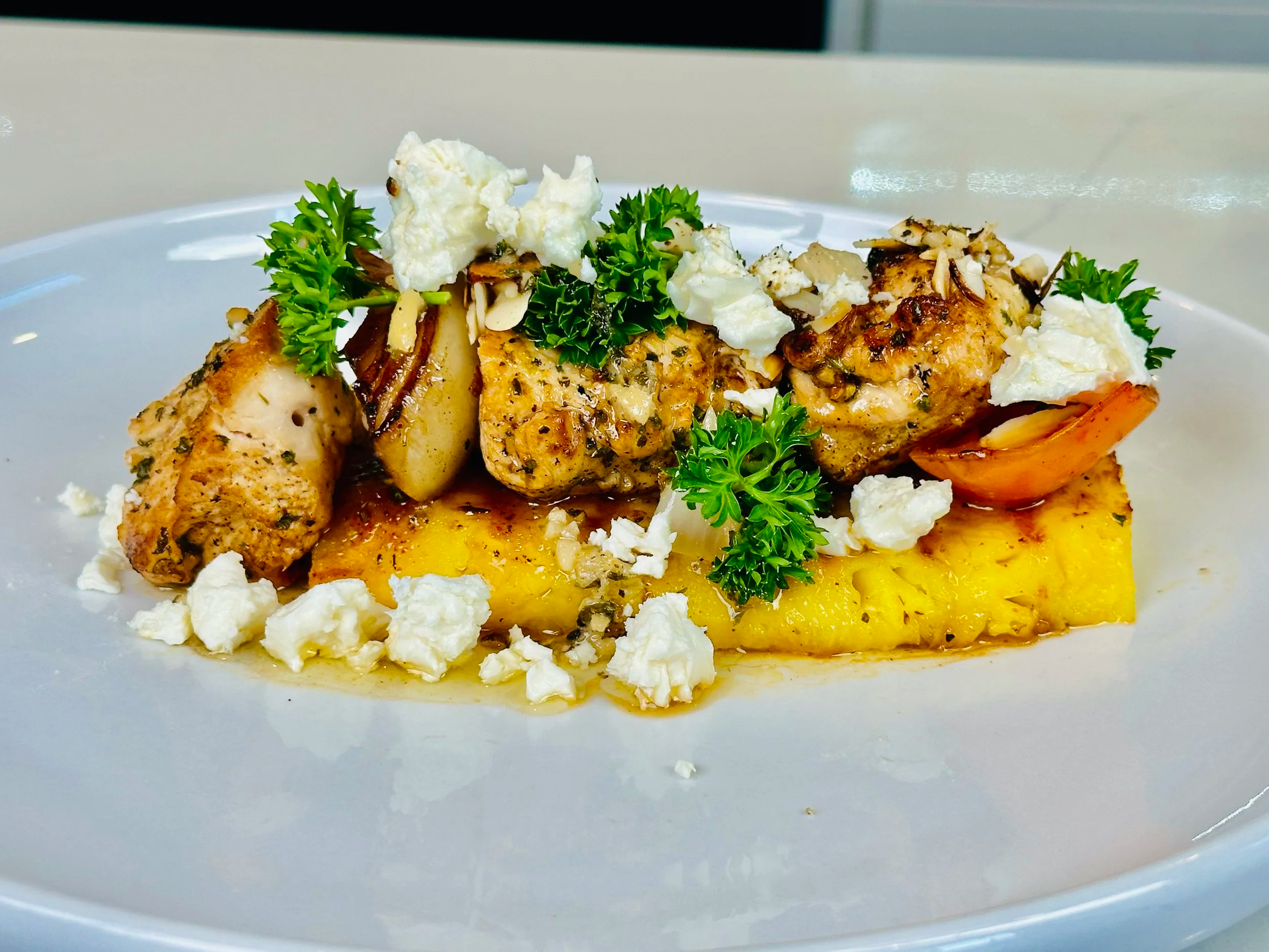 Plate of grilled chicken, roasted potatoes, garnished with parsley, crumbled cheese, and herbs on a white dish.
