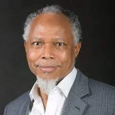 Portrait of Engr. Bayo Adeola  - Executive Chair of Comprehensive Project Management Services Lagos Nigeria - wearing a gray suit jacket and white shirt, against a dark background.
