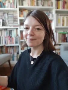 Person with brown hair smiling in front of a bookshelf filled with books.