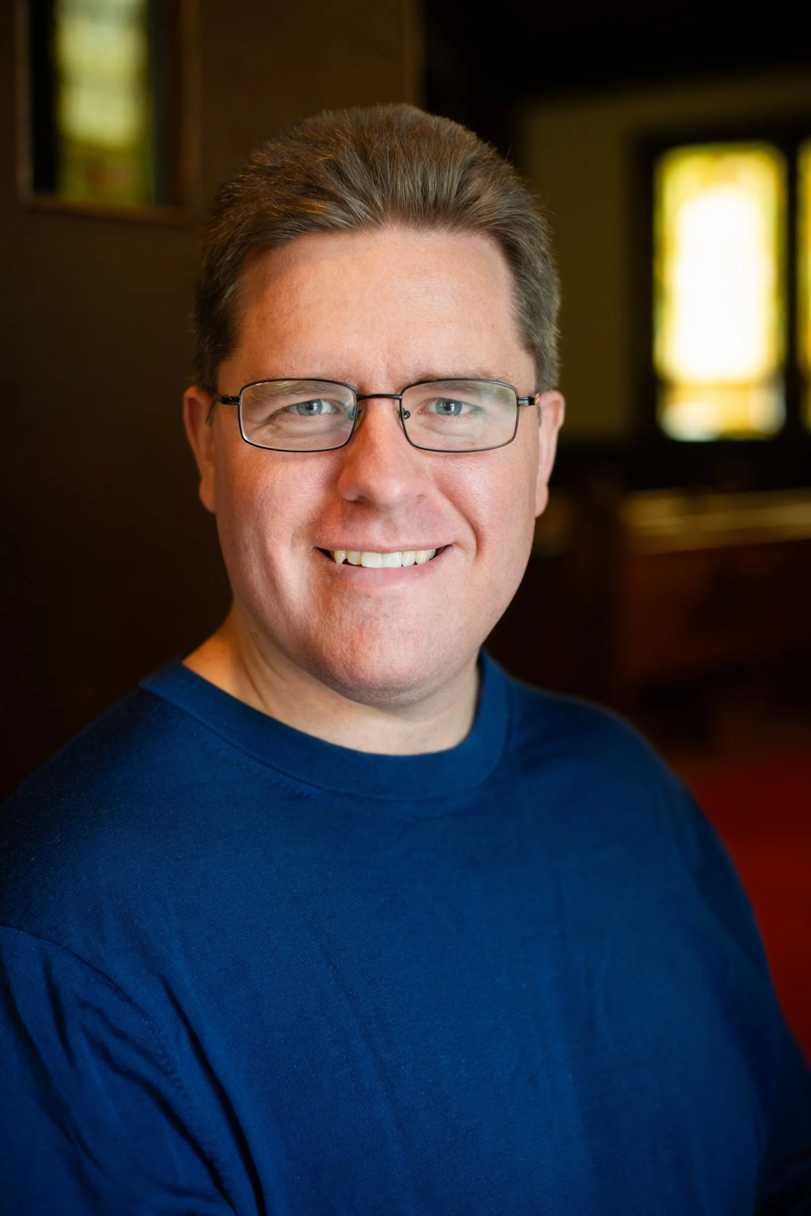 A man with glasses and a beard smiling at the camera outdoors.