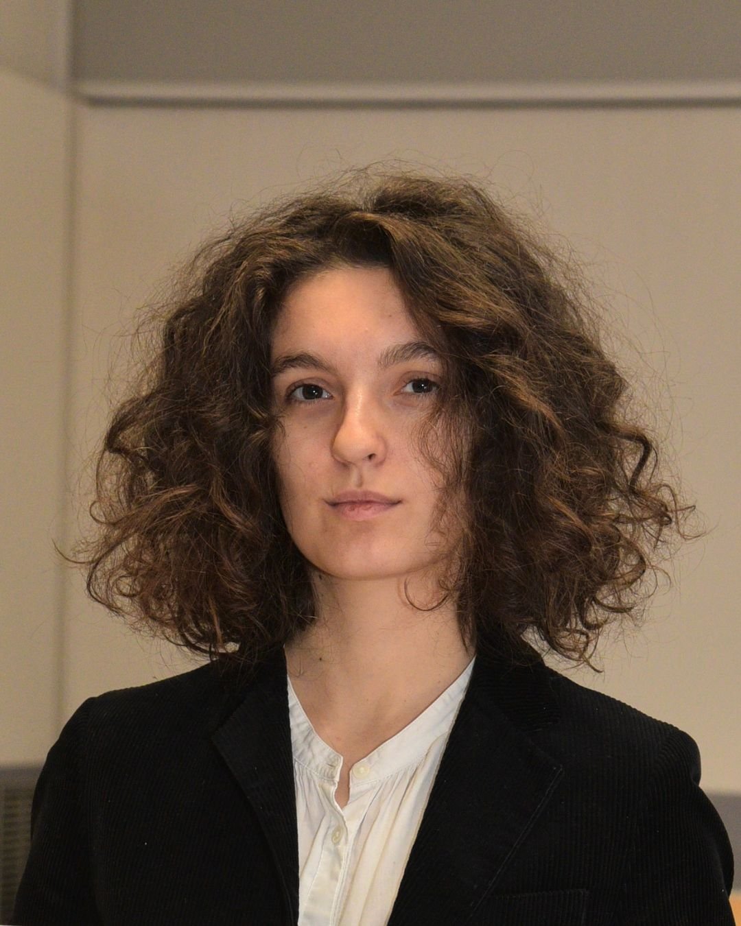 Ritratto di una giovane donna con capelli ricci, indossa una giacca nera e una camicia bianca.