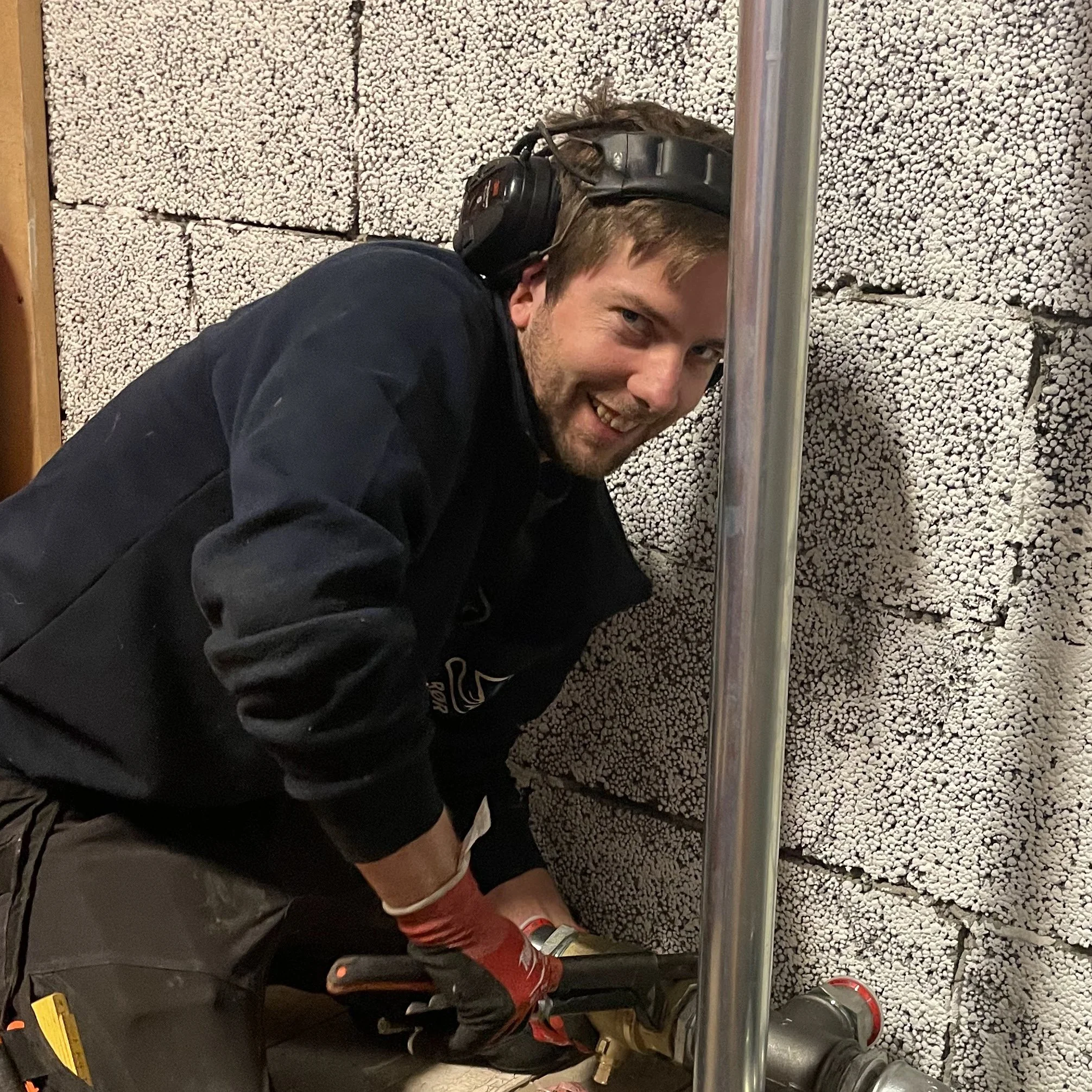 En mann med hjelm og arbeidsklær, som bruker verktøy for å arbeide med en vegg av isolasjonsmateriale.