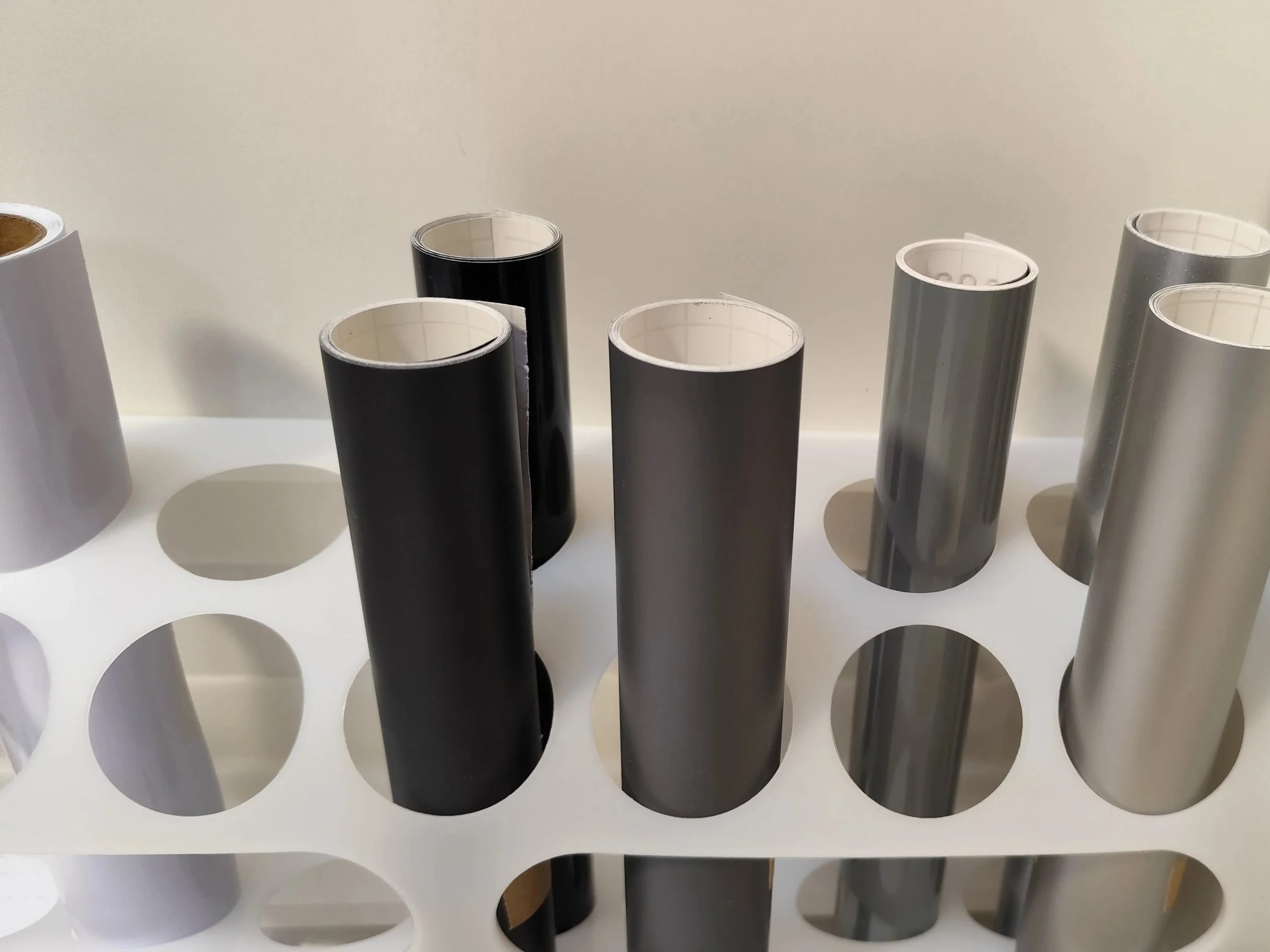 Mehrere Rollen mit schwarzem, silbernem und grauem Glanz in einem weißen Ständer