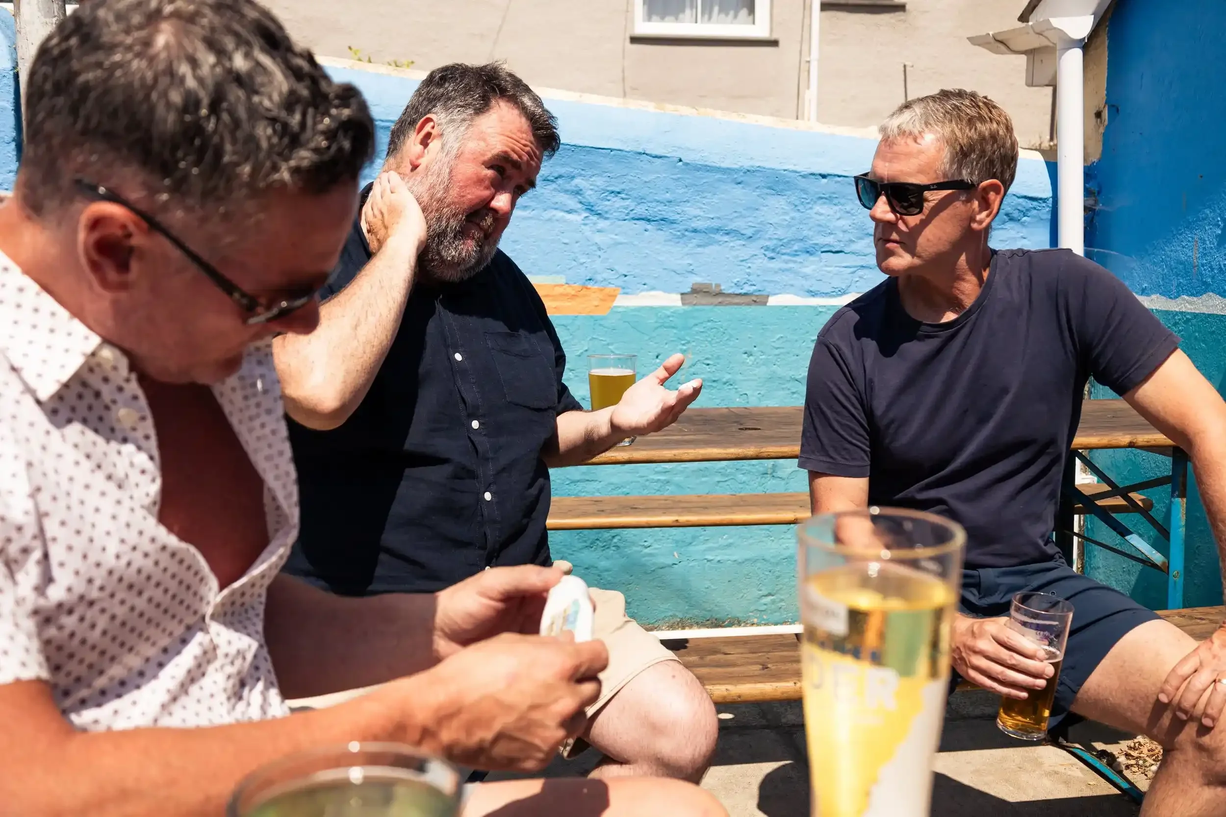Three men talking over drinks in a sunny beer garden at the Seaview Inn, from Matthew Morgan’s 'Proper Pub' documentary series.