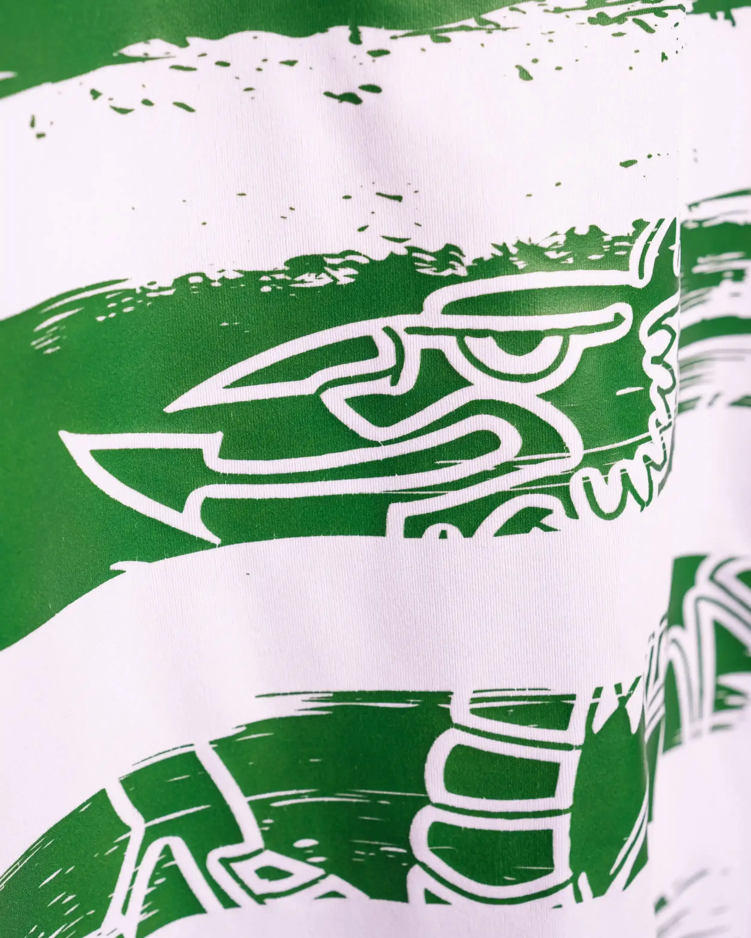 A macro close-up of The New Saints FC (TNS) home shirt fabric. The image shows horizontal green and white stripes with a detailed, white-lined abstract graphic resembling a shield or eagle integrated into the green sections. The fabric texture is vis