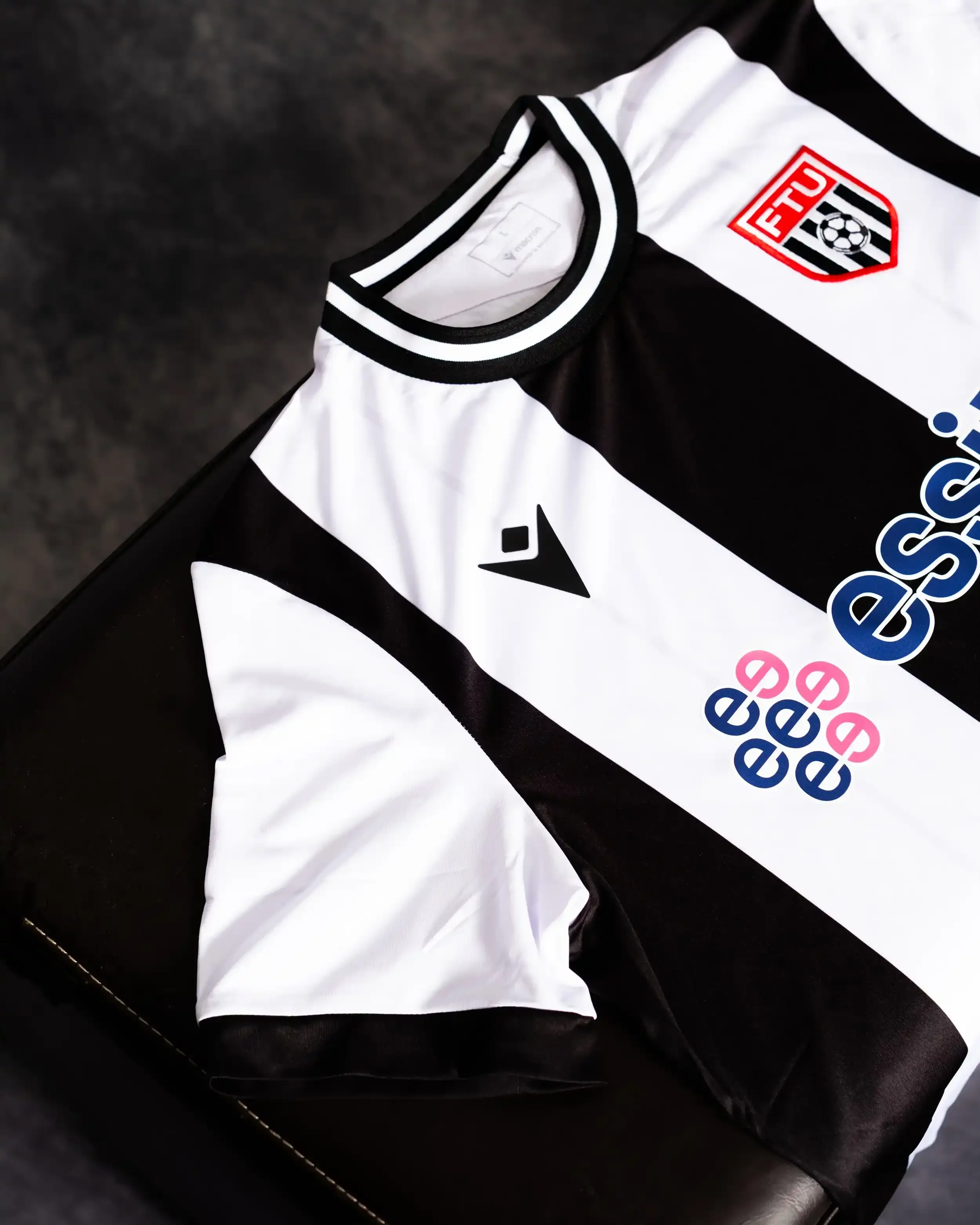 A professional product shot of the Flint Town United FC home shirt. The jersey features traditional wide black and white vertical stripes with a ribbed black and white crew neck collar. The FTU club crest is visible on the upper left chest, with the 
