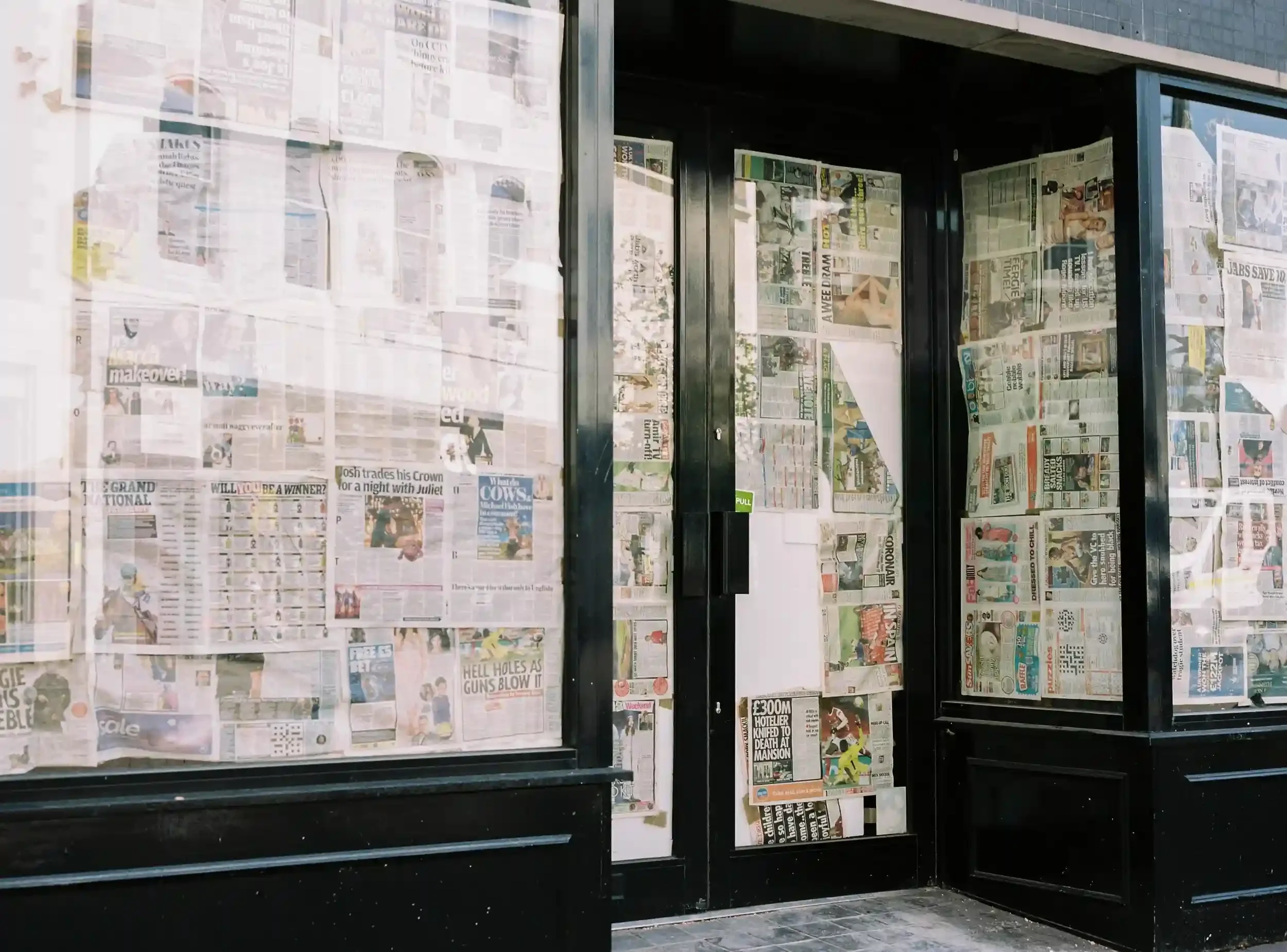A street-level view of a closed shop in Hereford with its large glass windows and doors completely covered from the inside with various newspaper pages during the 2021 lockdown, by Matthew Morgan.
