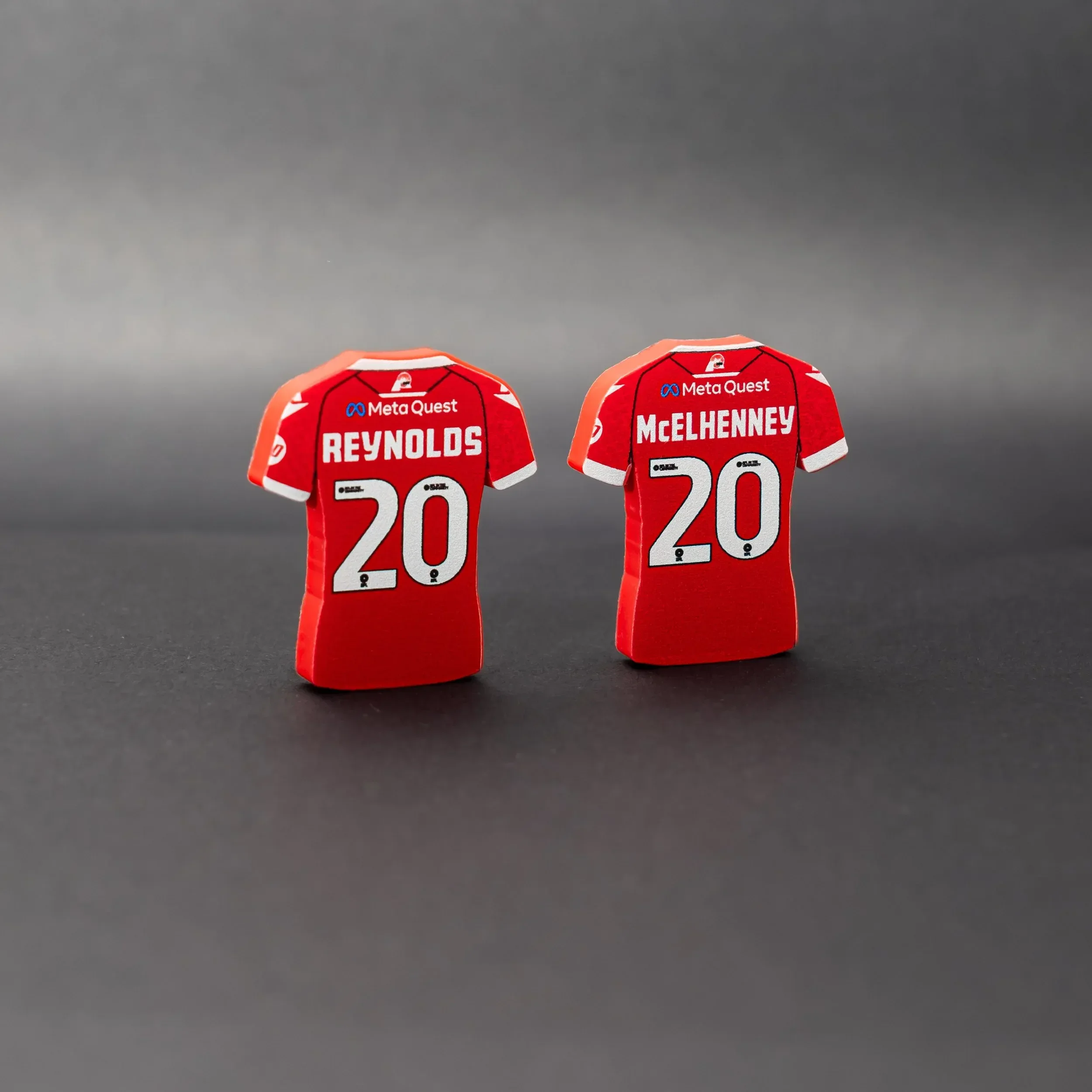 A professional studio shot of two custom Wrexham AFC home jersey tactical magnets by Your Game Your Name. The magnets are shown from the back, displaying red jerseys with white names and numbers. The left magnet features 'REYNOLDS' and the number '20