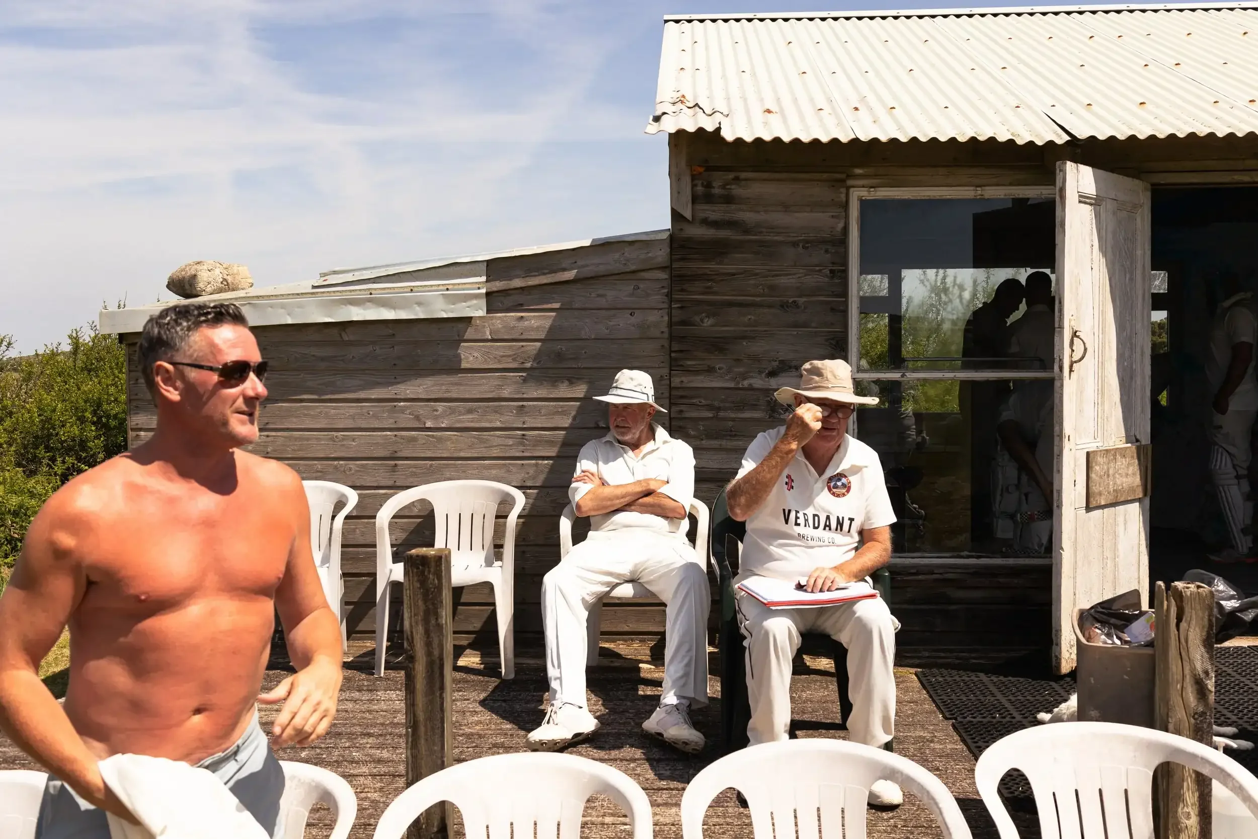 A shirtless cricketer, Damo, at the crease during a summer match at Nancledra Cricket Ground. Part of the 2024 award-winning 'Seaview Old Boys' sports series by Matthew Morgan.