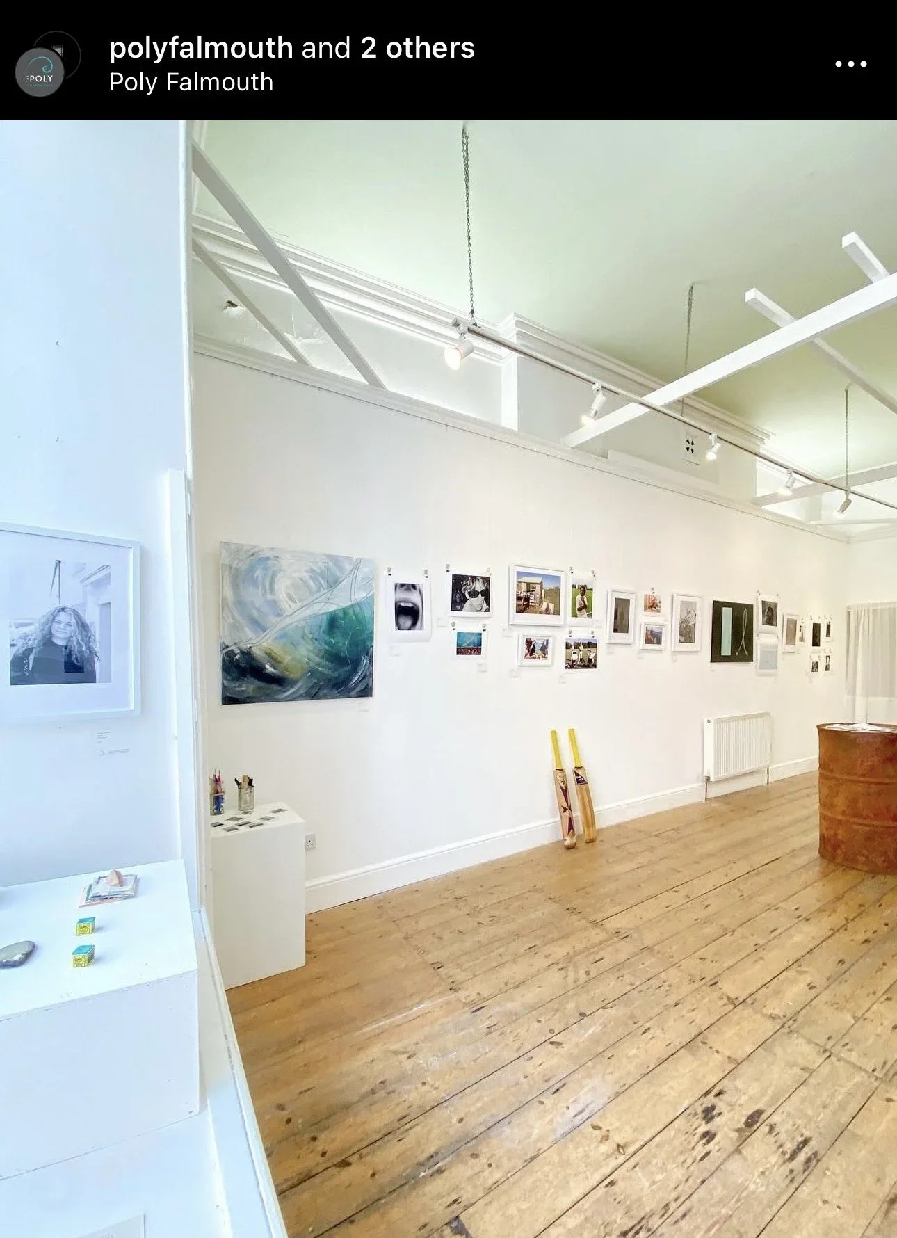 A bright, wide-angle interior view of an art gallery at The Poly in Falmouth. The white walls are lined with a diverse range of framed photographs, paintings, and smaller prints from the '2021-2024' exhibition by Matthew Morgan and Finlay Cummins. In
