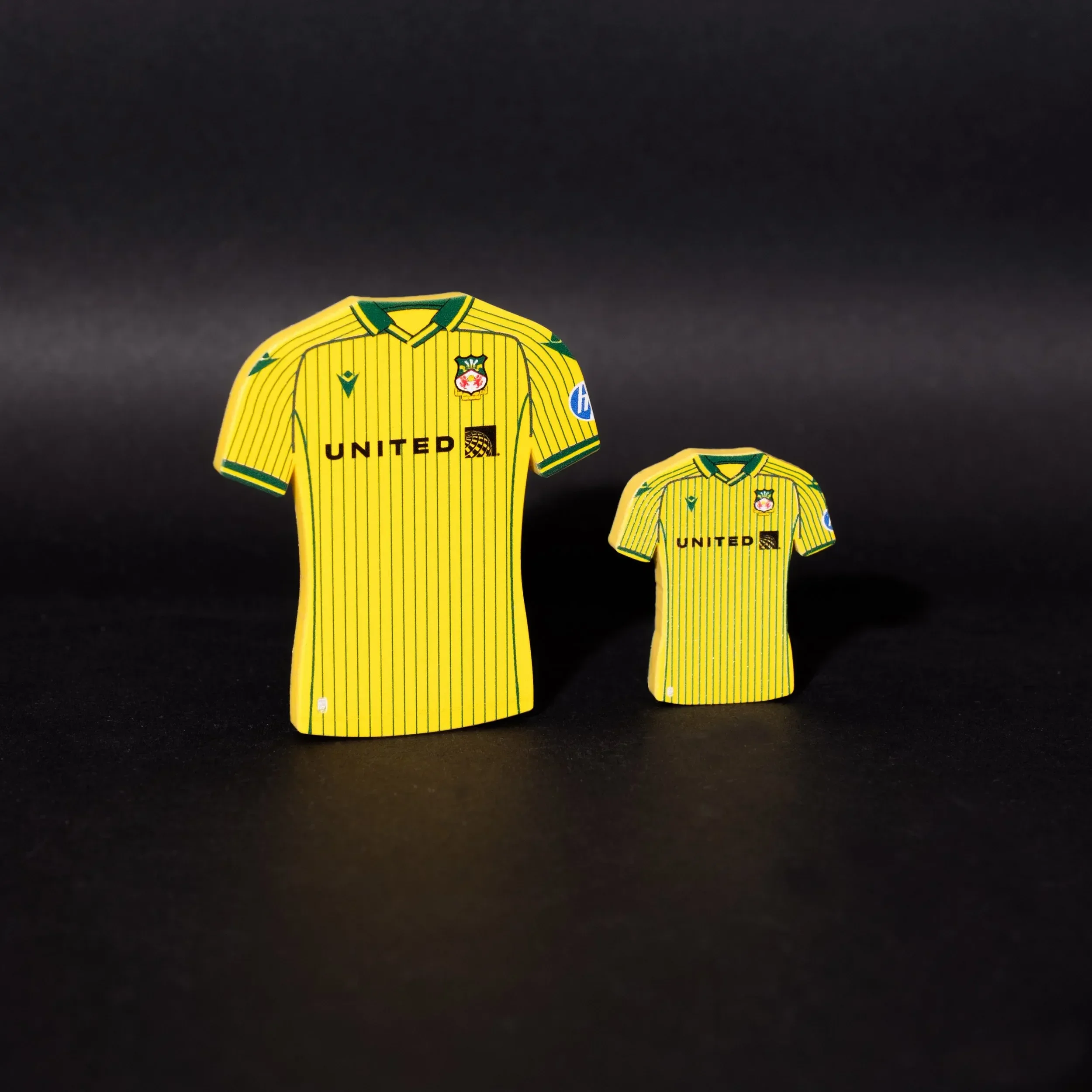 A professional product photograph of two Wrexham AFC away kit tactical magnets standing against a black background. The magnets are shaped like the club's yellow away jersey with green pinstripes and green collar detailing. Both the Wrexham AFC crest