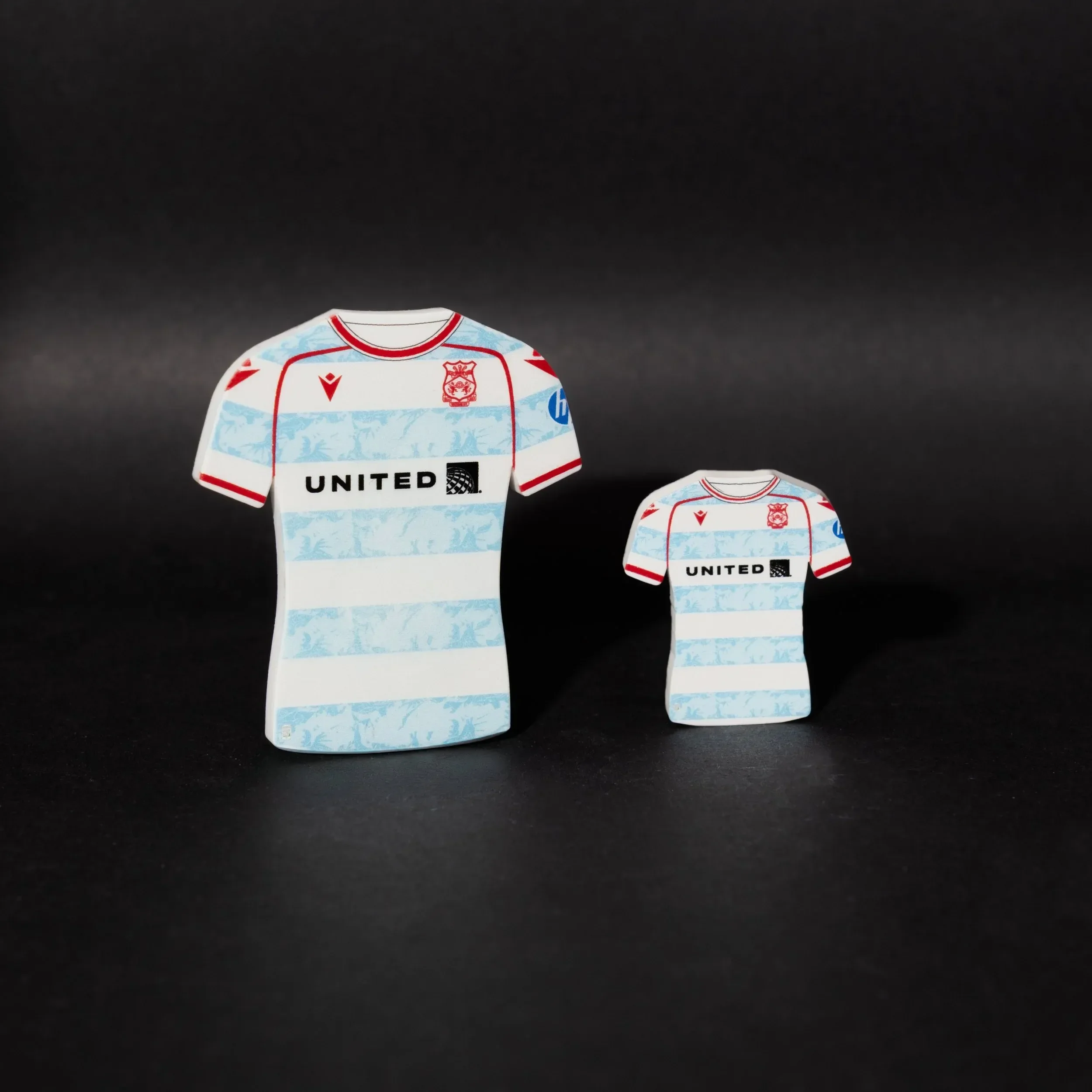 A clean studio photograph of two Wrexham AFC third kit tactical magnets by Your Game Your Name, set against a solid black background. The magnets are shaped like the official white away/third jersey, featuring blue patterned horizontal stripes, a red