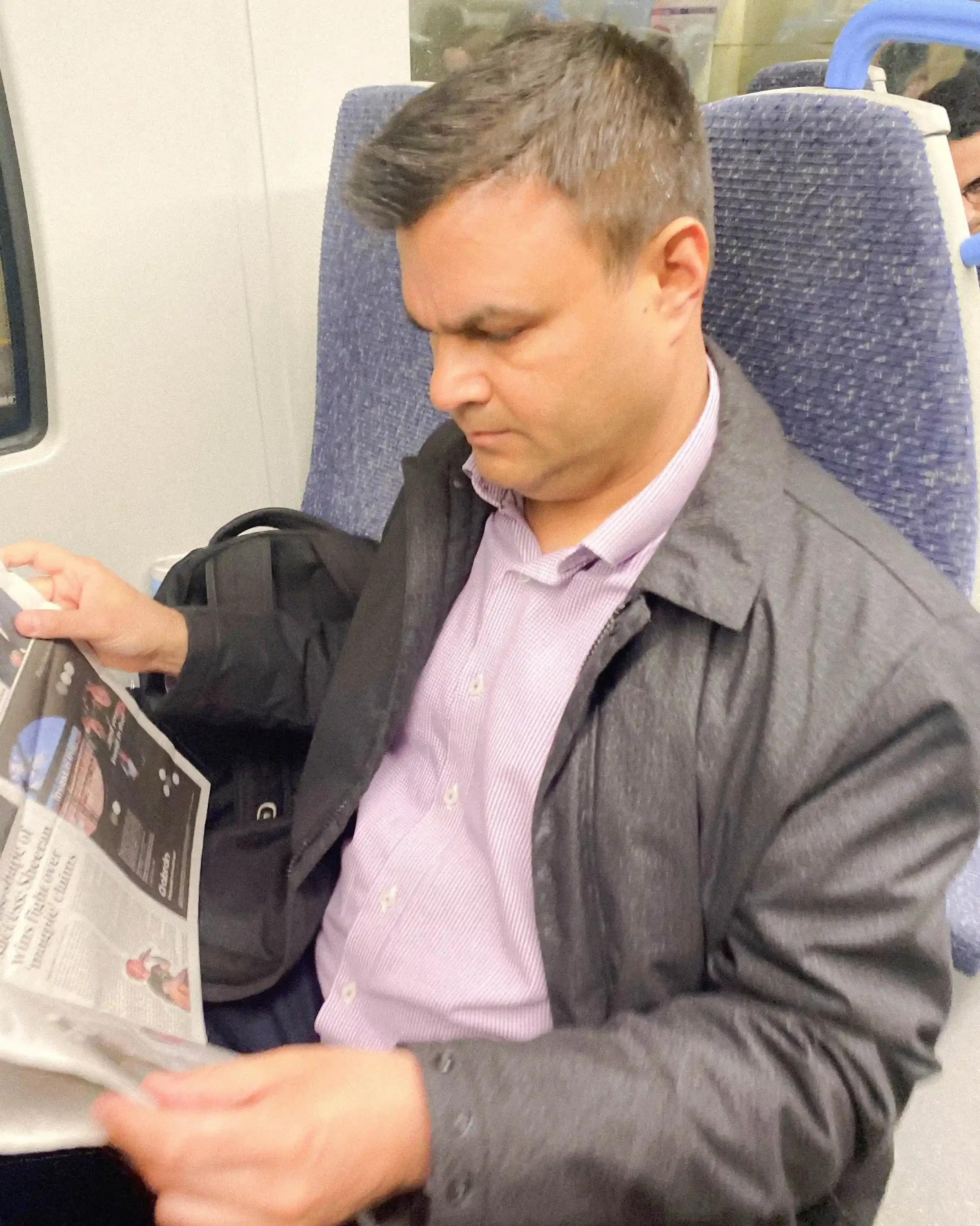 A man reading a free newspaper on a London Underground train, captured by Matthew Morgan for his 2022 series 'London's Free Newspapers'.