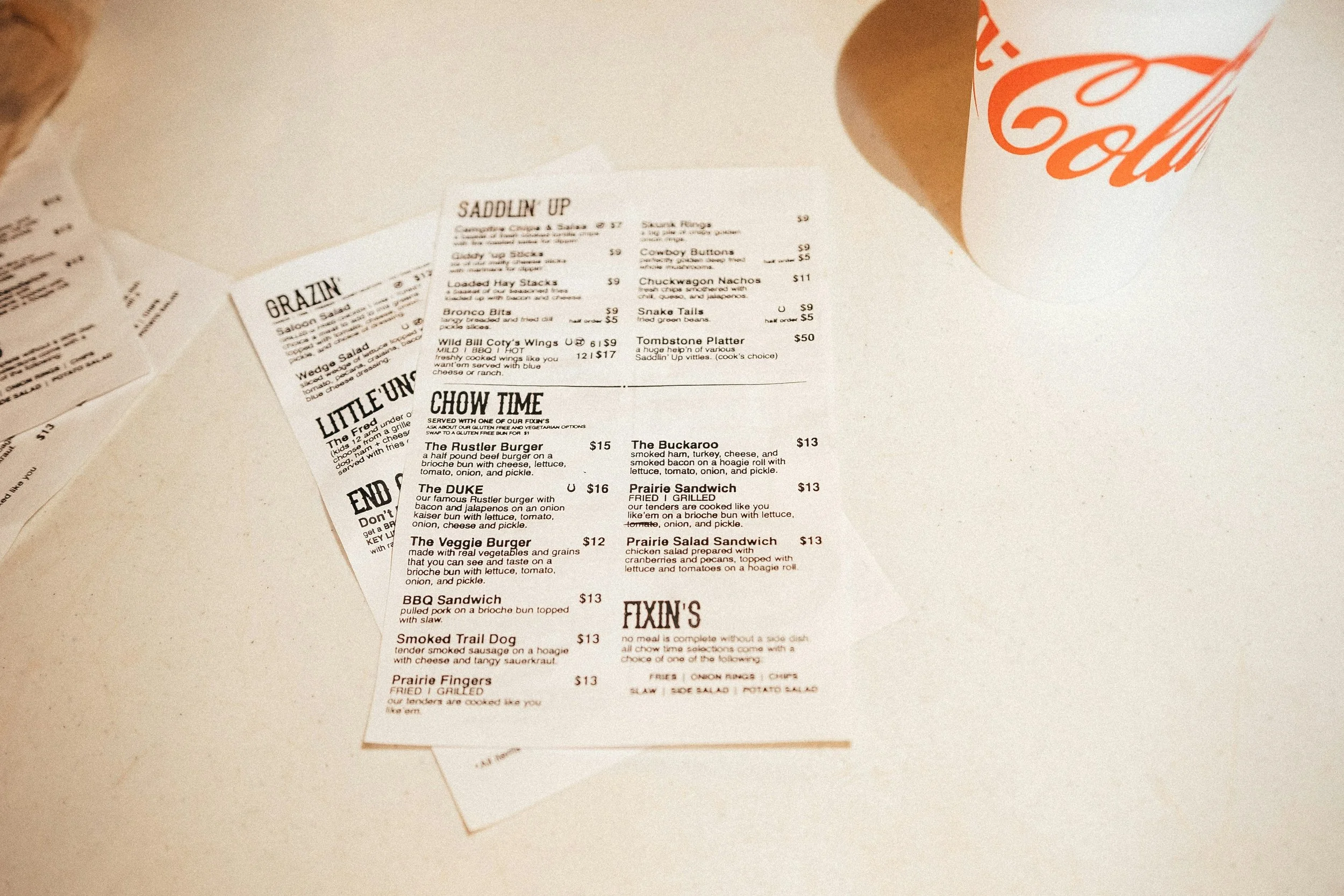 Letter sized menu for am ambiguous burger restaurant on a white table with a coca cola soda cup in view