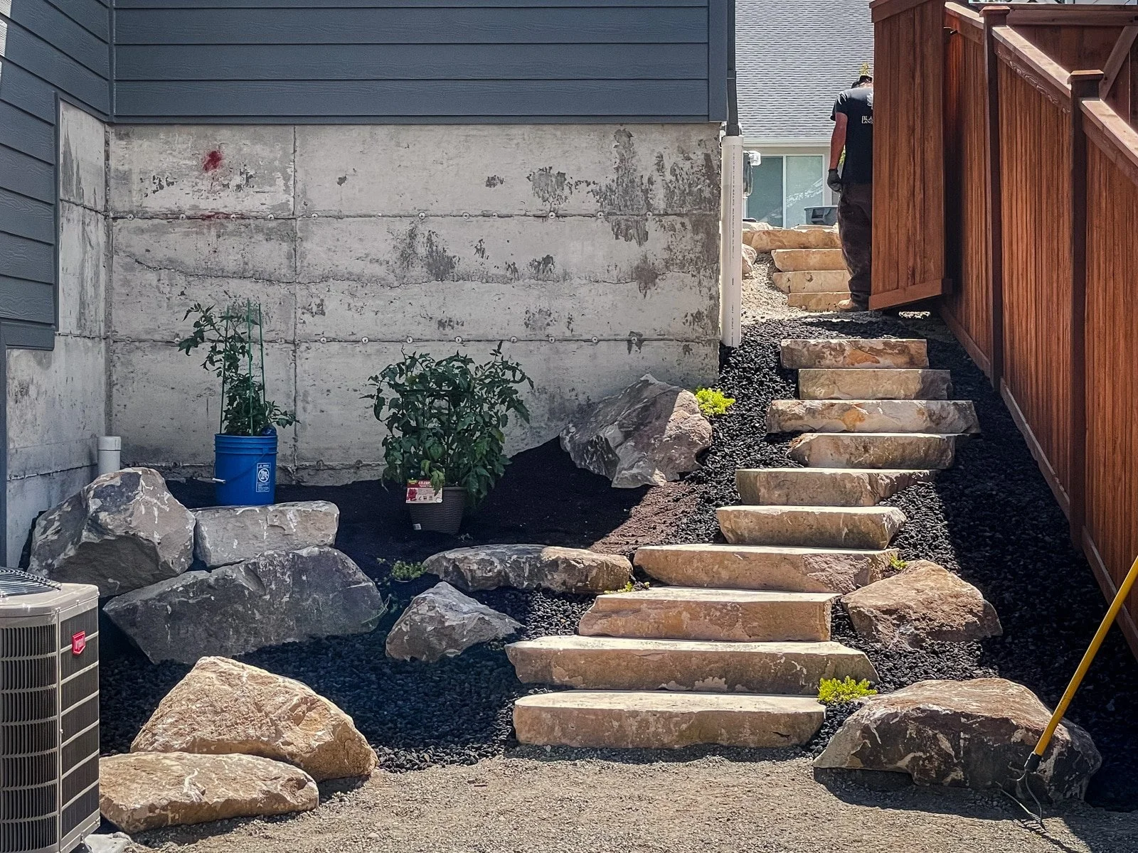 Large placement rocks, stone stairs, and a cedar fence.