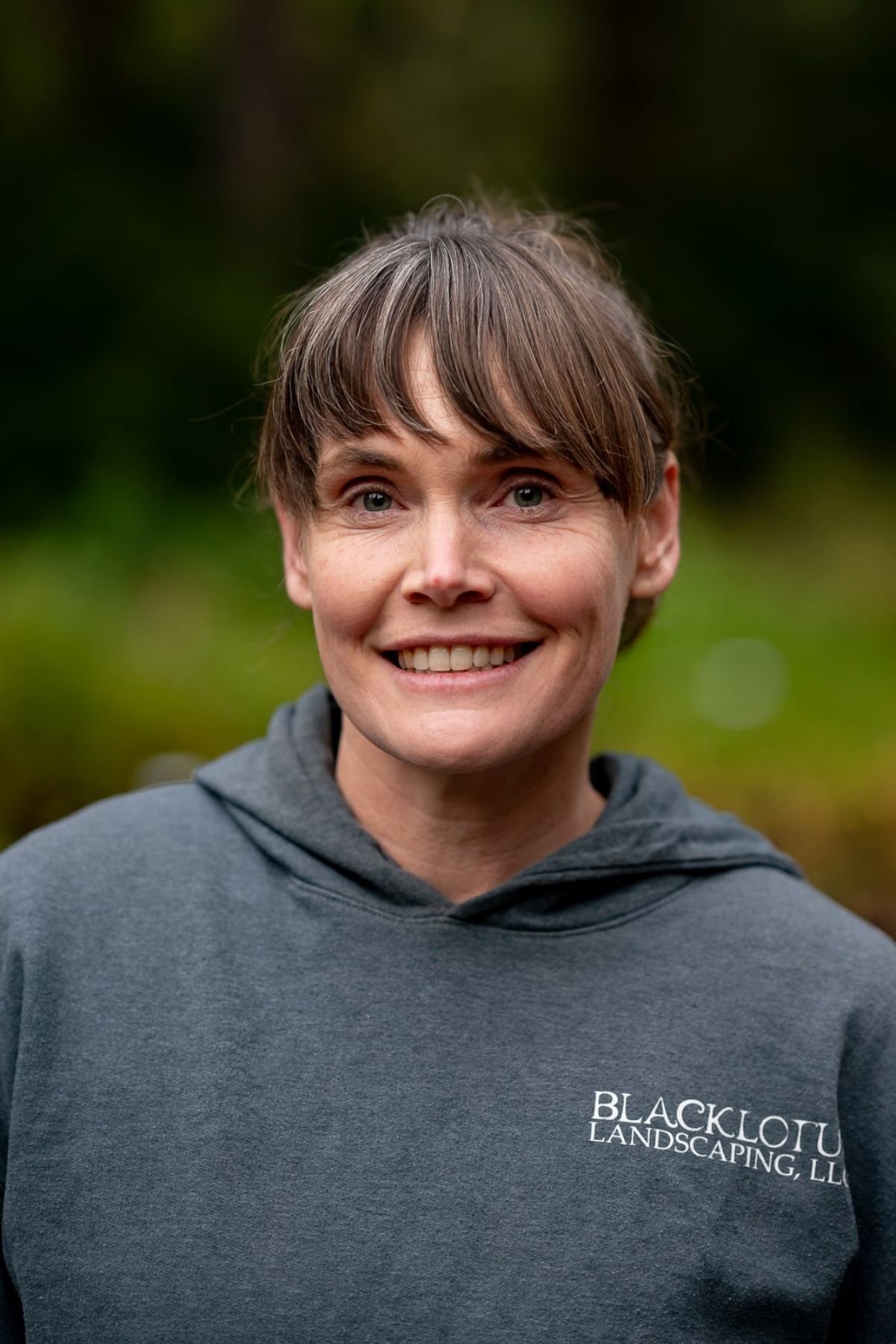 Woman smiling, standing in front of plants.
