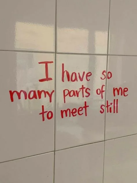 Quote on a tiled wall, "I have so many parts of me to meet still" written in red. 
