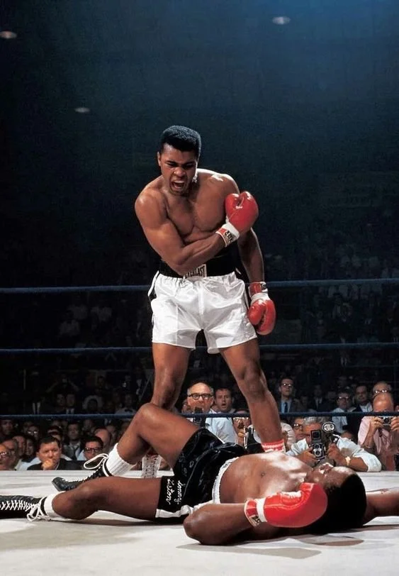 Boxer standing over opponent in boxing ring, wearing red gloves and white trunks.