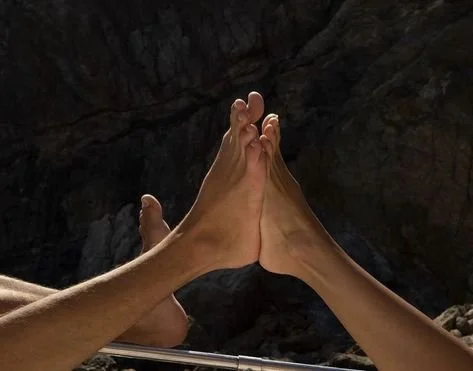 two feet pressing against each other with a rocky background