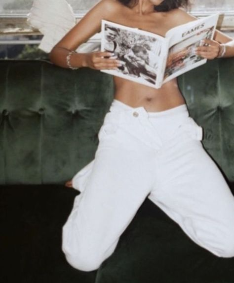 Person in white pants reading a magazine on a green sofa